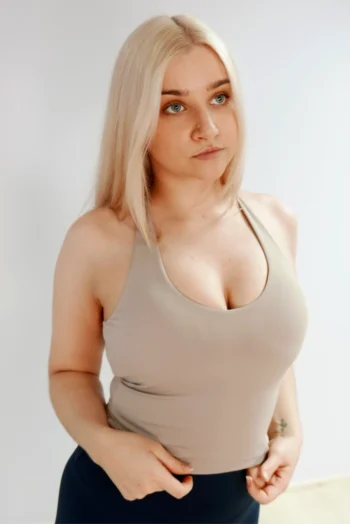 Foto kujutab heledate juustega naist, kes kannab beežikas-halli (taupe) toonis treeningtoppi.