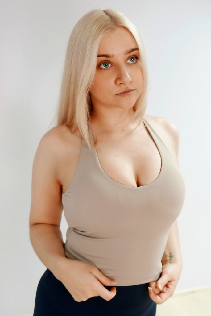 Foto kujutab heledate juustega naist, kes kannab beežikas-halli (taupe) toonis treeningtoppi.